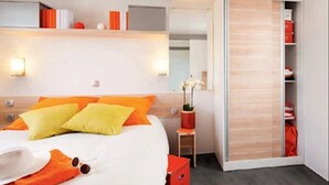 Ein modernes Hotelzimmer mit einem Bett, einem Nachttisch, einem Spiegel, einem Kleiderschrank und einem kleinen Tisch mit Blumen.