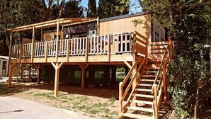 Una terraza de madera con una escalera que lleva a un segundo nivel, rodeada de árboles.