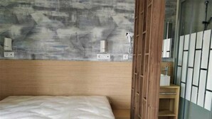 Un dormitorio con cama, cabecera de madera, aire acondicionado de pared y baño visible a través de una puerta de cristal.