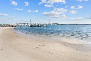 A beach with a pier extending into calm waters, sandy shore, and a clear sky.