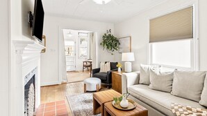 A living room with a sofa, a coffee table, a TV, and a fireplace. - Walk to Sound + Dining | Fenced Yard | Extended Stays Welcome Pet Friendly (Morehead City)