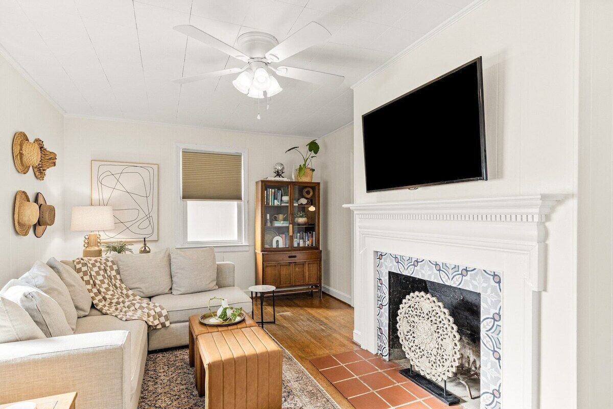 A living room with a sofa, a coffee table, a fireplace, a television, and a ceiling fan.