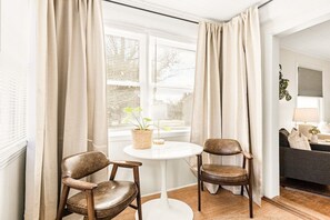 A room with two leather chairs, a white round table, a potted plant, and a sofa in the background.