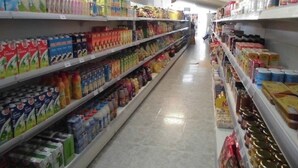 Un pasillo de supermercado con estantes llenos de diversos productos, entre ellos bebidas, aperitivos y artículos para el hogar.