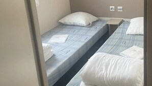 Une petite chambre d’hôtel composée d’une seule pièce, avec deux lits simples, une tête de lit et une petite table.