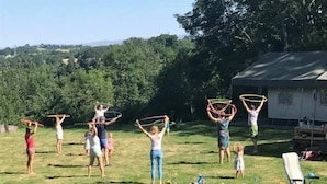 Un groupe d’enfants joue avec des cerceaux de hula hoop dans un espace extérieur enherbé, avec une maison en arrière-plan.