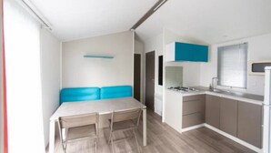 A compact kitchen with a dining area, a gas stove, and a window with blinds. - ZEcamping 4 étoiles 500m plage espace aquatique chiens acceptés locatif TV (Benodet)