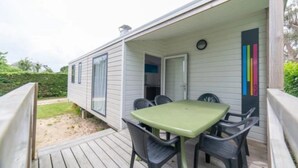 A mobile home with a wooden deck, a green table, and four chairs. - ZEcamping 4 étoiles 500m plage espace aquatique chiens acceptés locatif TV (Benodet)