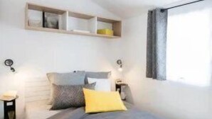 A modern bedroom with a bed, bedside tables, and a window. - ZEcamping 4 étoiles familial 500m plage espace aquatique locatif TV (Benodet)
