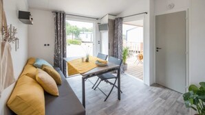 A modern living room with a sofa, a dining table, and a view to an outdoor deck. - ZEcamping 4 étoiles familial 500m plage espace aquatique locatif TV (Benodet)