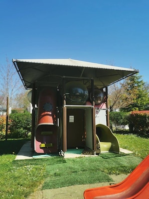 A playground with slides and a covered playhouse structure.