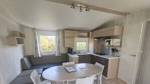 A compact kitchen with a dining area, a built-in bench, and a window providing natural light. - ZEcamping 3 étoiles pataugeoire animaux acceptés fitness locatif TV 34m2 (Pouldreuzic)