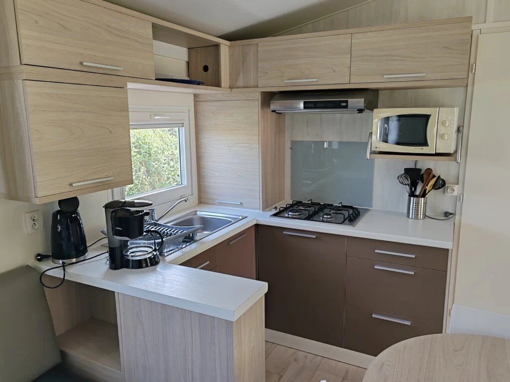 Een kleine keuken met een magnetron, fornuis, koffiezetapparaat en een raam dat voor natuurlijk licht zorgt.
