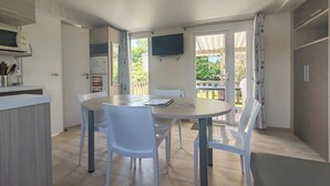 A kitchen with a dining table and chairs, a TV on the wall, and a sliding glass door leading to an outdoor area. - ZEcamping 3 étoiles pataugeoire animaux acceptés fitness locatif TV 34m2 (Pouldreuzic)