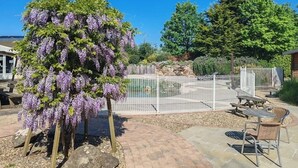 Un espacio al aire libre cercado con un pérgola cubierta de flores moradas, una piscina y mesas de picnic.