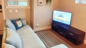 Een woonkamer met een bank, een flatscreen televisie, een kleine plant en een ingelijste foto aan de muur.
