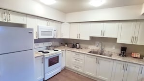 Een moderne keuken met witte kastjes, een ingebouwde magnetron, fornuis, oven en een spoelbak.