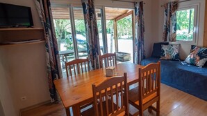 Un comedor con una mesa y sillas de madera, un televisor en un estante y un sofá con cojines estampados.