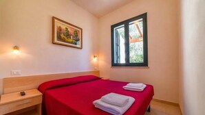 Ein Schlafzimmer mit zwei Betten, einem Bild an der Wand und einem Fenster mit Blick auf Grünflächen.