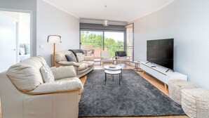 Ein modernes Wohnzimmer mit einer Couch, einem Couchtisch, einem Fernseher und einem Balkon mit Blick.