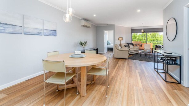 Ein modernes Wohnzimmer mit einem runden Holzesstisch, beigen Sofas und einem schwarzen Couchtisch.