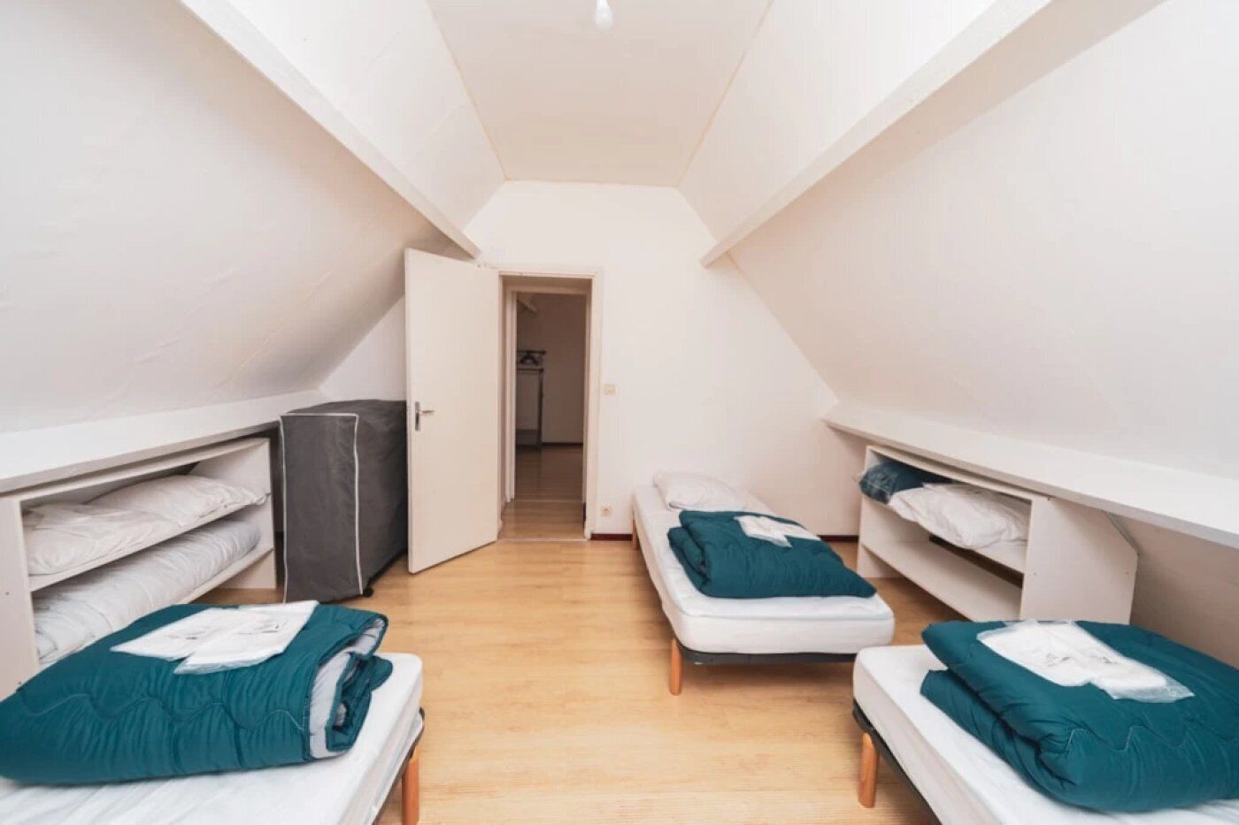 A dormitory room with two single beds, a wardrobe, and a door leading to another room.