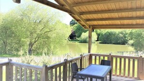 A wooden deck with a table and chairs overlooking a lake. - ZEcamping 3 étoiles animé piscine chauffée dog friendly hammam locatif TV LV (Merdrignac)