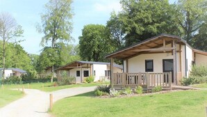 A row of single-story cabins with a porch, surrounded by greenery and trees. - ZEcamping 3 étoiles animé piscine chauffée dog friendly hammam locatif TV LV (Merdrignac)