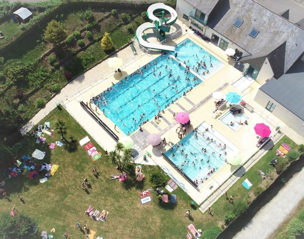 A large outdoor swimming pool with multiple lanes, surrounded by sun loungers and umbrellas.