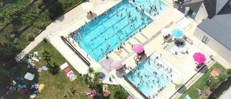 A large outdoor swimming pool with multiple lanes, surrounded by sun loungers and umbrellas.