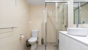 Un baño moderno con inodoro, cabina de ducha de vidrio y lavabo con espejo.