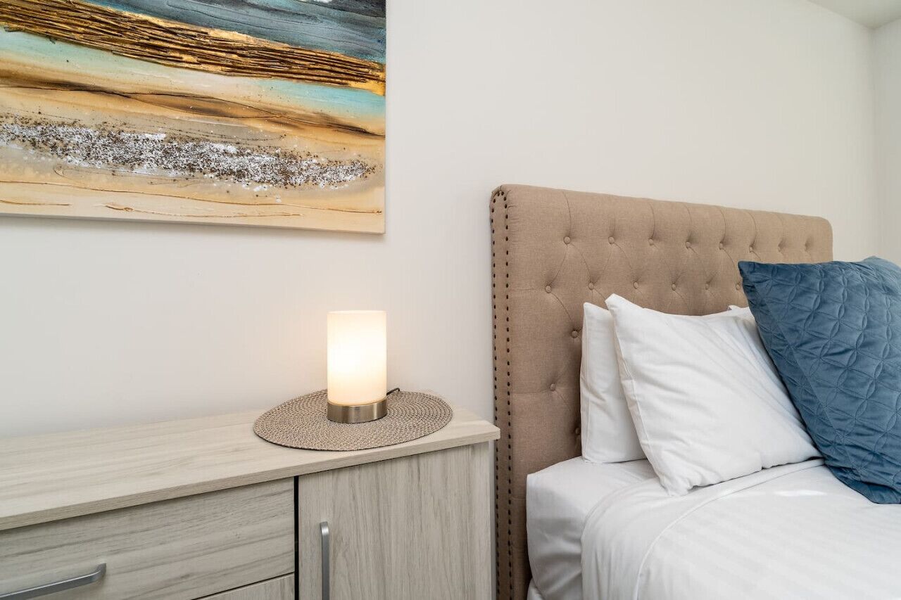 Een slaapkamer met een bed, een nachtkastje met lamp, een schilderij aan de muur, en een nachtkastje.