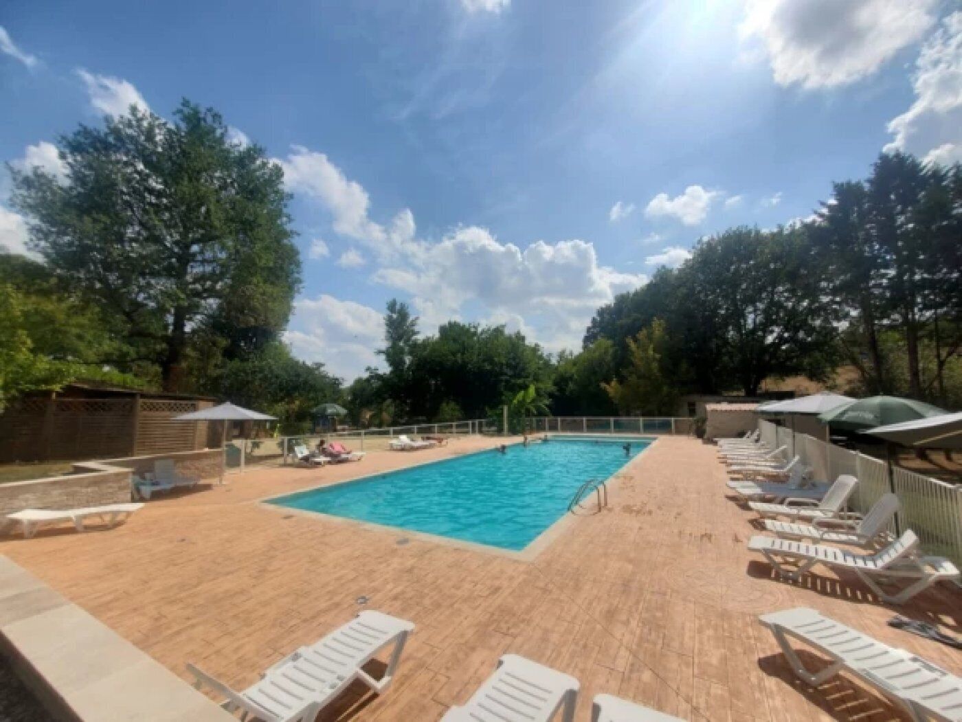 Ein rechteckiger Swimmingpool mit umlaufender Holzterrasse, ausgestattet mit Liegestühlen und Sonnenschirmen.
