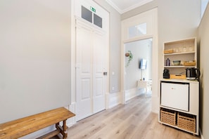 A hallway with a bench, a white door with an exit sign, a small kitchenette with a coffee maker, and a plant.