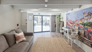 A hotel lobby with a sofa, a rug, a painting, and a view of the street outside. - GuestReady - Alegria 293 - Room 1 (Porto)