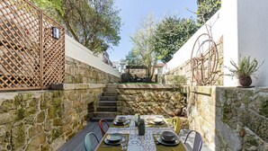 Un espacio de comedor al aire libre con paredes de piedra, una mesa de madera dispuesta con platos, vasos y cubiertos, y sillas.