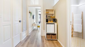 Un pasillo con puertas blancas, una pequeña kitchenette con cafetera y un piso a cuadros.