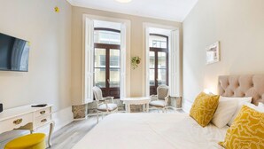 A hotel room with a bed, a desk, two chairs, a television, and large windows. - GuestReady - Alegria 293 - Room 1 (Porto)
