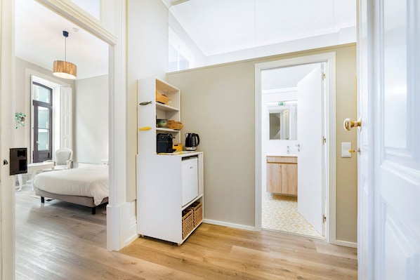 A hotel room with a bed, a white wardrobe, a small table, and a door leading to a bathroom.