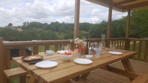 Eine Holzterrasse mit Esstisch, umgeben von einem Holgitter, mit Blick auf ein bewaldetes Gebiet.