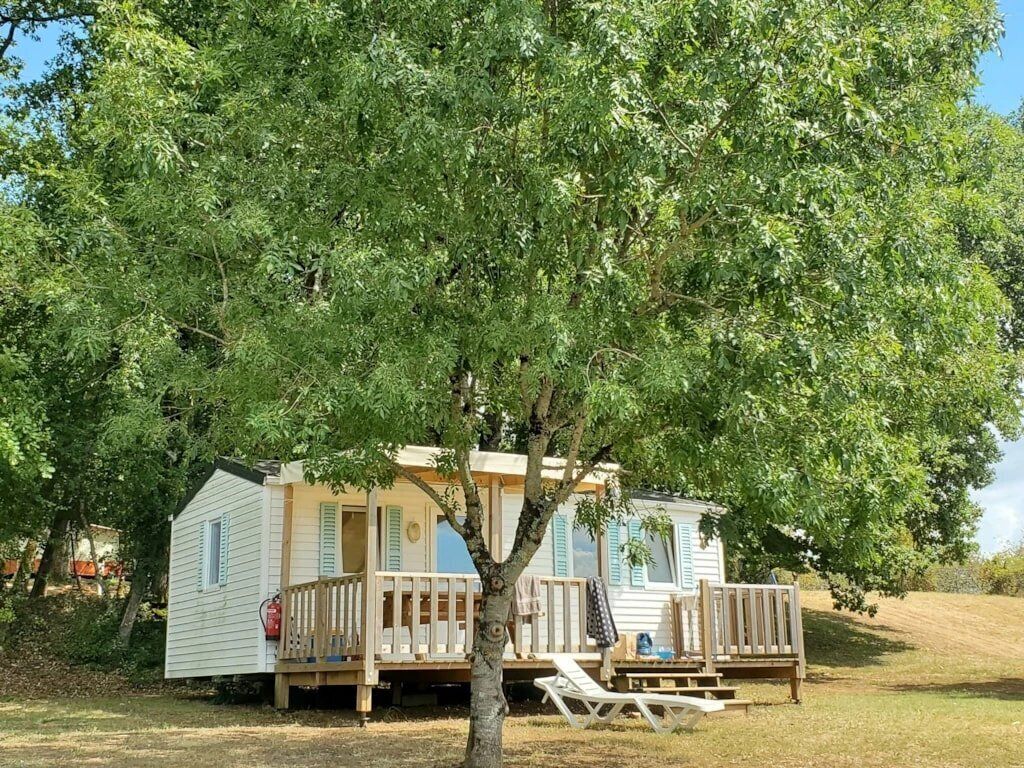 Une maison mobile avec une terrasse, un arbre devant et une table de pique-nique.