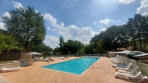 Una piscina con sillas de descanso y sombrillas, rodeada de árboles y una terraza de madera.