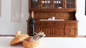 A wooden cabinet with glass doors, a wine bottle, and two baskets on a white floor. - Casa Duesse (IUN R6224)Accommodation located in the very center of Orosei. (Orosei)