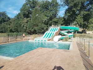 A swimming pool with a water slide, surrounded by trees.
