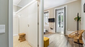 A modern hotel room with a wooden floor, a yellow ottoman, a wicker chair, and a TV mounted on the wall. - GuestReady - Alegria 293 - Room 2 (Porto)