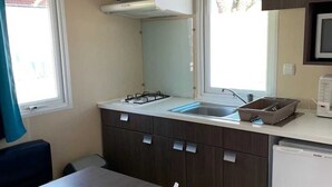 Una kitchenette compacta con estufa a gas, pileta y microondas. Hay una mesa de comedor con sillas y una ventana que proporciona luz natural.