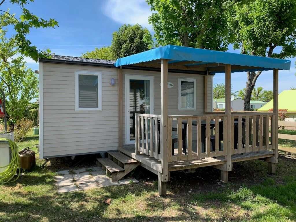 Une petite maison mobile dotée d’une terrasse en bois et d’un auvent bleu.