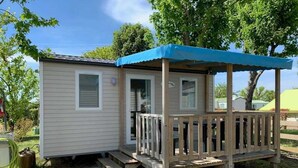 Una casa rodante pequeña con una terraza de madera y un toldo azul.