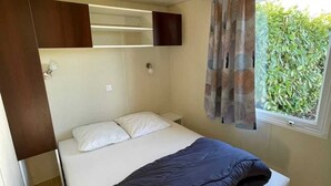 Une chambre à coucher de taille modeste, comprenant un lit, une petite table de chevet, une étagère intégrée et une fenêtre avec des rideaux.