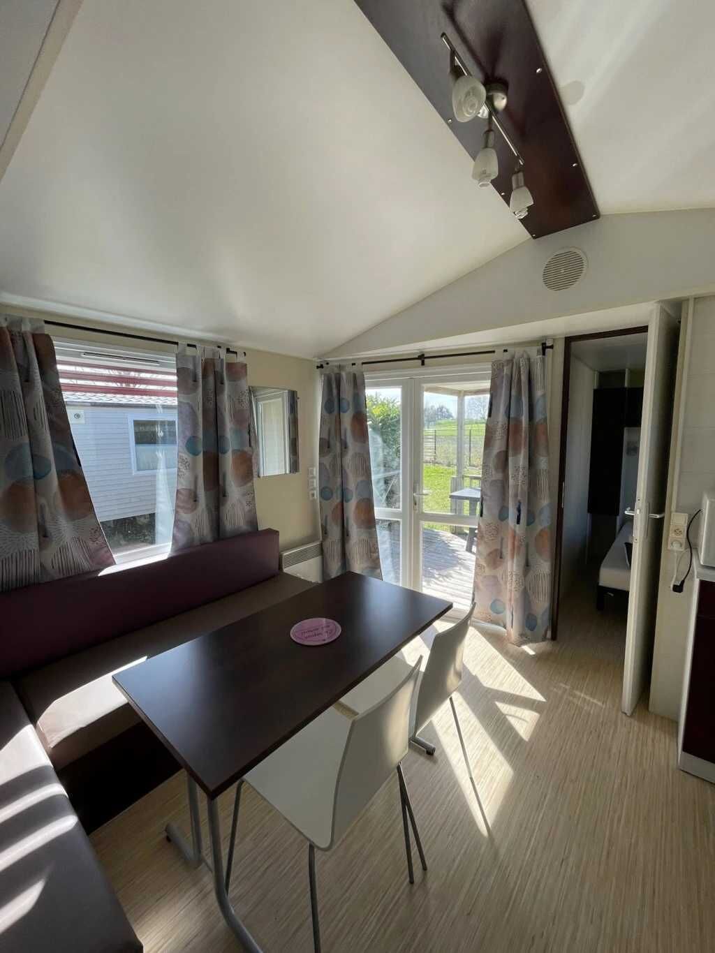 A cozy room with a dark wooden table, white chairs, a cushioned bench, and a view of the outdoors through a sliding door.